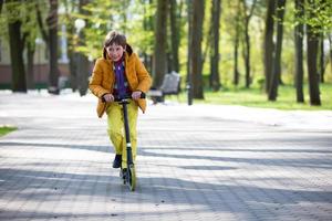 el niño paseos un scooter en el parque. un chico en brillante ropa obras de teatro un primavera día. foto