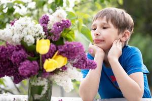 Beautiful child with a bouquet of lilacs. Boy look at the flowers. photo