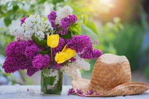 Spring or summer background. A bouquet of lilacs and straw panama lit by sunlight. Beautiful flowers on a green background. photo