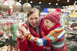 mamá con un niño a el Navidad venta. alegre los compradores a el Navidad mercado escoger productos foto