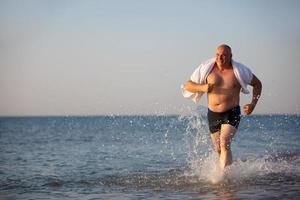 un mayor hombre carreras a lo largo el playa. foto