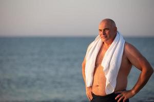 Elderly handsome man with a white towel on a background of the sea. photo