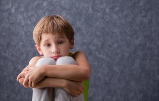 A sad child sits hugging his knees. A boy of elementary age is sad. Schoolboy detuned on a gray background. photo