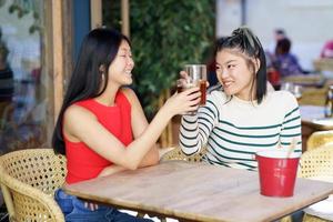 alegre asiático mujer tintinamente lentes de frío té en café foto