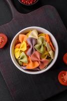 Raw farfalle pasta in different colors on a dark concrete background photo