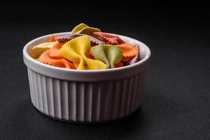 Raw farfalle pasta in different colors on a dark concrete background photo