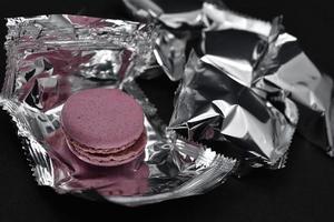 Macaroons on a shiny wrapper. Colorful delicious macaroons on a black background. Shiny cookie wrapper. photo