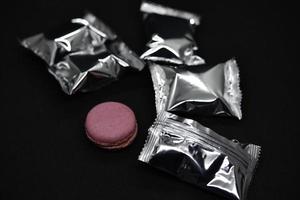 Macaroons on a shiny wrapper. Colorful delicious macaroons on a black background. Shiny cookie wrapper. photo