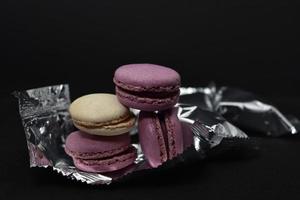 Macaroons on a shiny wrapper. Colorful delicious macaroons on a black background. Shiny cookie wrapper. photo