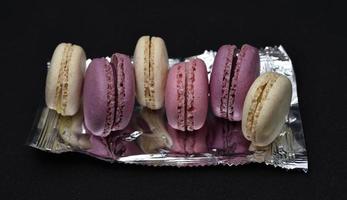 Macaroons on a shiny wrapper. Colorful delicious macaroons on a black background. Shiny cookie wrapper. photo