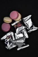 Macaroons on a shiny wrapper. Colorful delicious macaroons on a black background. Shiny cookie wrapper. photo
