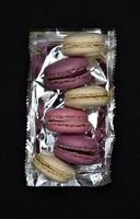 Macaroons on a shiny wrapper. Colorful delicious macaroons on a black background. Shiny cookie wrapper. photo