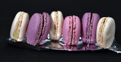 Macaroons on a shiny wrapper. Colorful delicious macaroons on a black background. Shiny cookie wrapper. photo