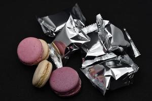 Macaroons on a shiny wrapper. Colorful delicious macaroons on a black background. Shiny cookie wrapper. photo