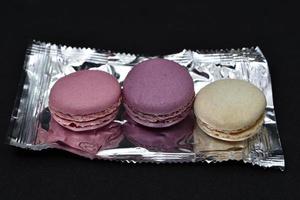 Macaroons on a shiny wrapper. Colorful delicious macaroons on a black background. Shiny cookie wrapper. photo