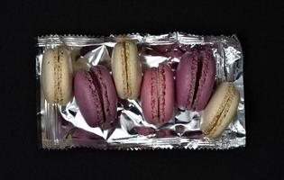 Macaroons on a shiny wrapper. Colorful delicious macaroons on a black background. Shiny cookie wrapper. photo