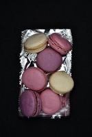 Macaroons on a shiny wrapper. Colorful delicious macaroons on a black background. Shiny cookie wrapper. photo