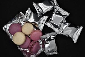 Macaroons on a shiny wrapper. Colorful delicious macaroons on a black background. Shiny cookie wrapper. photo