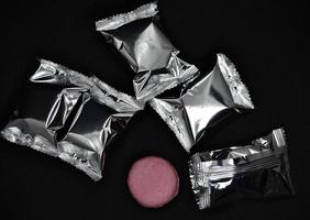 Macaroons on a shiny wrapper. Colorful delicious macaroons on a black background. Shiny cookie wrapper. photo