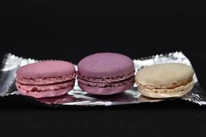 Macaroons on a shiny wrapper. Colorful delicious macaroons on a black background. Shiny cookie wrapper. photo