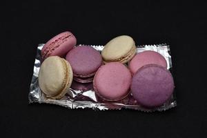 Macaroons on a shiny wrapper. Colorful delicious macaroons on a black background. Shiny cookie wrapper. photo