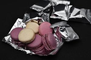 Macaroons on a shiny wrapper. Colorful delicious macaroons on a black background. Shiny cookie wrapper. photo