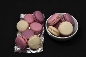 Macaroons on a shiny wrapper. Colorful delicious macaroons on a black background. Shiny cookie wrapper. photo