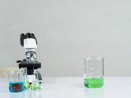 beaker and microscope for scientists was placed on a white wooden table with research reagents in the bright white room for study and work photo