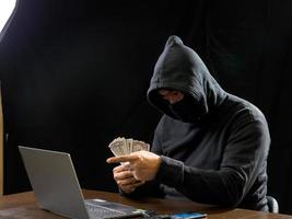 Hacker spy man one person in black hoodie sitting on a table looking computer laptop used login password attack security to circulate data digital in internet network system, night dark background. photo