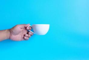 Man hand holding a white coffee cup, filled with hot black coffee americano, no sugar no milk, ready to drink, refreshing. aroma awake fresh to work placed on a blue isolated background photo