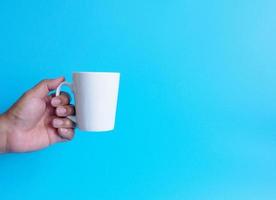 mano de hombre sosteniendo una taza de café con leche, llena de café negro caliente americano, sin azúcar ni leche, lista para beber, refrescante. aroma despierto fresco para trabajar colocado sobre un fondo azul aislado foto