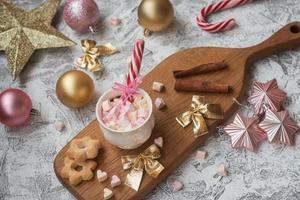 Taza de composición de año nuevo o navidad con marshmelow en un soporte de madera con galletas y dulces entre juguetes brillantes de año nuevo foto