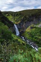 Cascade of mountain waterfall, high-mountain vegetation - green bushes and trees photo