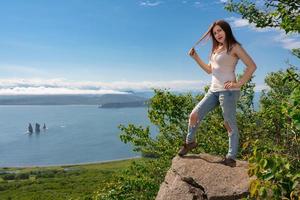 Adult woman standing on shore in mountains against panoramic of green forest and ocean on summer day photo