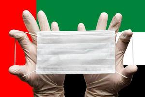 Medic holds face mask in hands on background of national flag of United Arab Emirates UAE. Concept photo