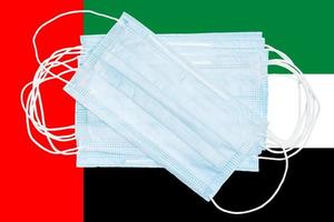 Lot of medical protective surgical face masks on background national colors flag of United Arab Emirates UAE. Concept of disease in country and global world photo
