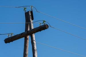 Old electricity pylon cables on wooden poles on blue sky photo