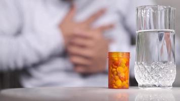 pill container and glass on water on table and man coughing on background video