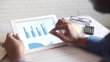Man's hand working on digital tablet at office desk, using self created chart video