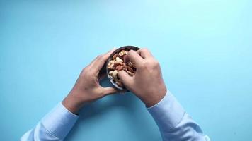top view of hand holding a bowl of mixed nut on blue background video
