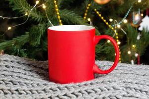 Blank red mug with christmas tree on background,mat tea or coffee cup with christmas and new year decoration,vertical mock up with ceramic mug for hot drinks,empty gift print template. photo