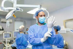 Portrait of male doctor surgeon putting on medical gloves standing in operation room. Surgeon at modern operating room photo