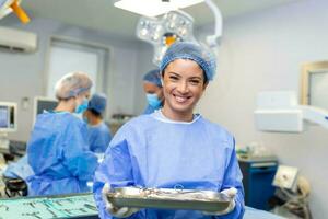 Portrait of female woman nurse surgeon OR staff member dressed in surgical scrubs gown mask and hair net in hospital operating room theater making eye contact smiling pleased happy looking at camera photo