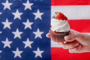 hand holding sweet cupcake with blueberries and strawberry , flag background photo