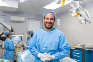 retrato de masculino enfermero cirujano o personal miembro vestido en quirúrgico matorrales vestido máscara y pelo red en hospital operando habitación teatro haciendo ojo contacto sonriente satisfecho contento mirando a cámara foto