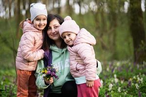 contento de la madre día. nosotros amor tú, mamá. madre con un ramo de flores de flores y dos hijas en primavera floreciente bosque. foto