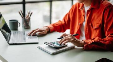 mujeres contando monedas en la calculadora sacando de la alcancía. mano que sostiene la pluma trabajando en la calculadora para calcular en el escritorio sobre el costo en la oficina en casa. foto