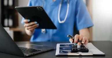 Healthcare costs and fees concept.Hand of smart doctor used a calculator and smartphone, tablet for medical costs at hospital in morning light photo