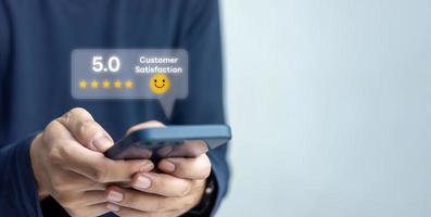 Customer service satisfaction evaluation concept. Man using smartphone and touching on screen with gold five star rating excellent feedback icon, Rated a very good review. photo