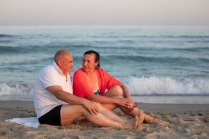 A middle-aged woman and man are sitting on a sandy shore against the background of the sea. Happy married couple at the resort. photo